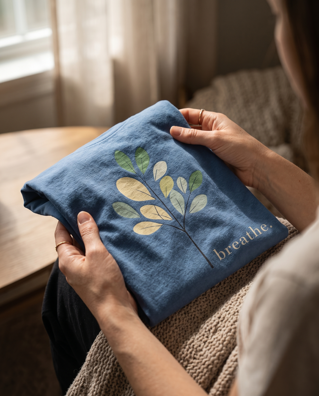 Close-up of hands gently holding a folded soft cotton “Breathe” t-shirt  in warm natural window light — the truth about natural fibers by Trees and Leaves